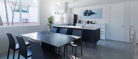 Una cocina moderna con una isla central, un comedor con mesa y sillas, y un amplio ventanal que aporta luz natural.