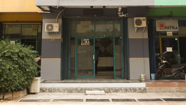 Un hôtel appelé « GRAND IORA », doté d’une façade moderne, de grandes fenêtres et d’un appareil de climatisation visible.