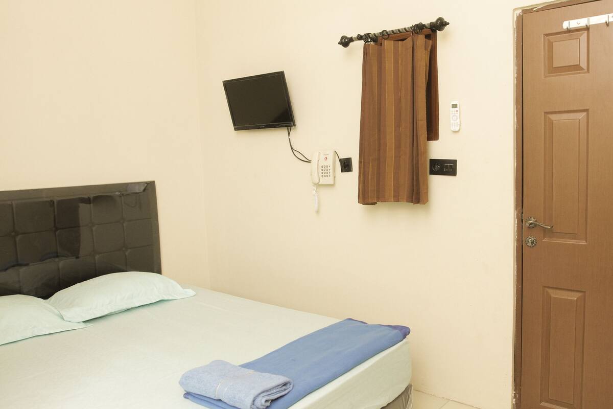 Una habitación de hotel con una cama, un televisor montado en la pared, un teléfono y una puerta.