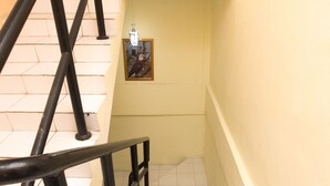 Un escalier avec des rampes noires et des carreaux blancs, menant à une pièce où un tableau encadré est accroché au mur.