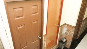 Une porte en bois avec une poignée en métal, un sol carrelé avec un motif imitant la pierre et une poubelle.