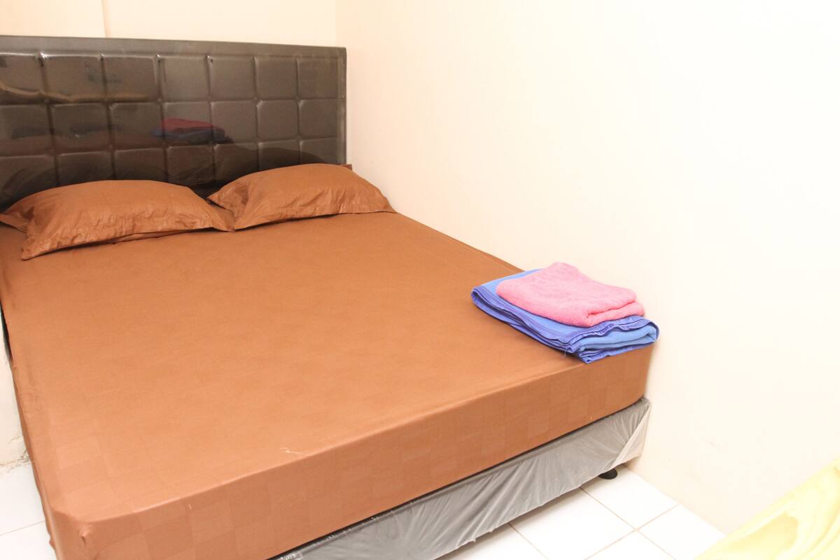 Una cama con colchón y almohadas marrones, cabecera y una manta doblada al pie.