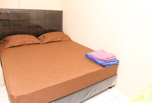 Ein Bett mit einer braunen Matratze und Kissen, einem Kopfteil und einer zusammengelegten Decke am Fußende.