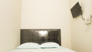 Une chambre d’hôtel avec un lit, une serviette pliée, un téléphone sur la table de chevet et une tablette fixée au mur.