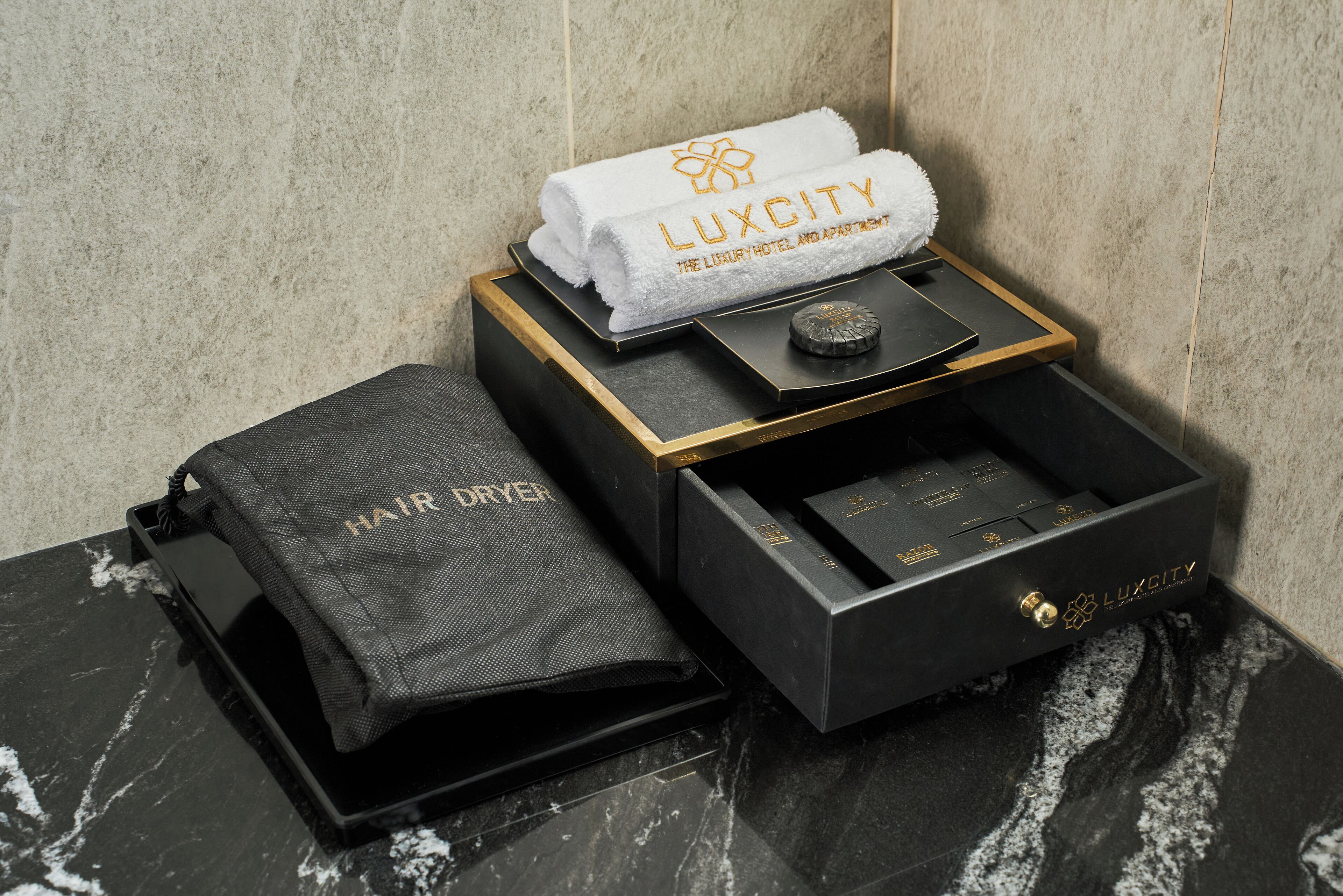 A luxury hotel bathroom with a marble countertop, a black and gold hair dryer, a towel, and a black box with a gold lock.