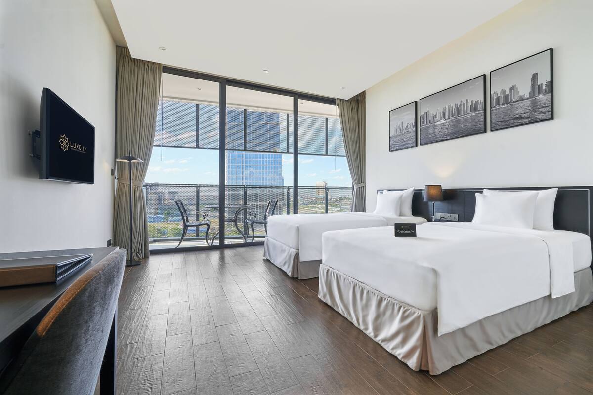 A hotel room with two beds, a TV, a balcony with a city view, and a desk.
