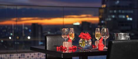 A table set for two with wine glasses, a vase with red roses, and a candle holder.