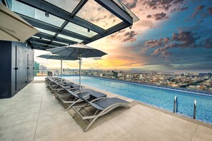 A rooftop pool area with lounge chairs and umbrellas, overlooking a cityscape at sunset. - Luxcity Hotel & Apartment (Phnom Penh)