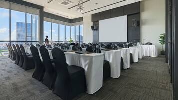 Un salón de conferencias con varias mesas, sillas negras y una pantalla grande.