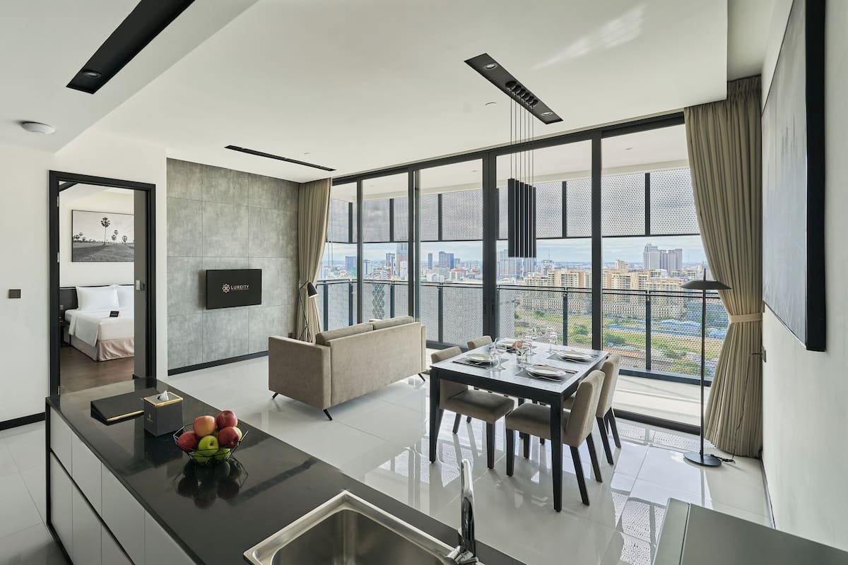 A modern living room with a dining area, a TV mounted on the wall, and a large window offering a city view.