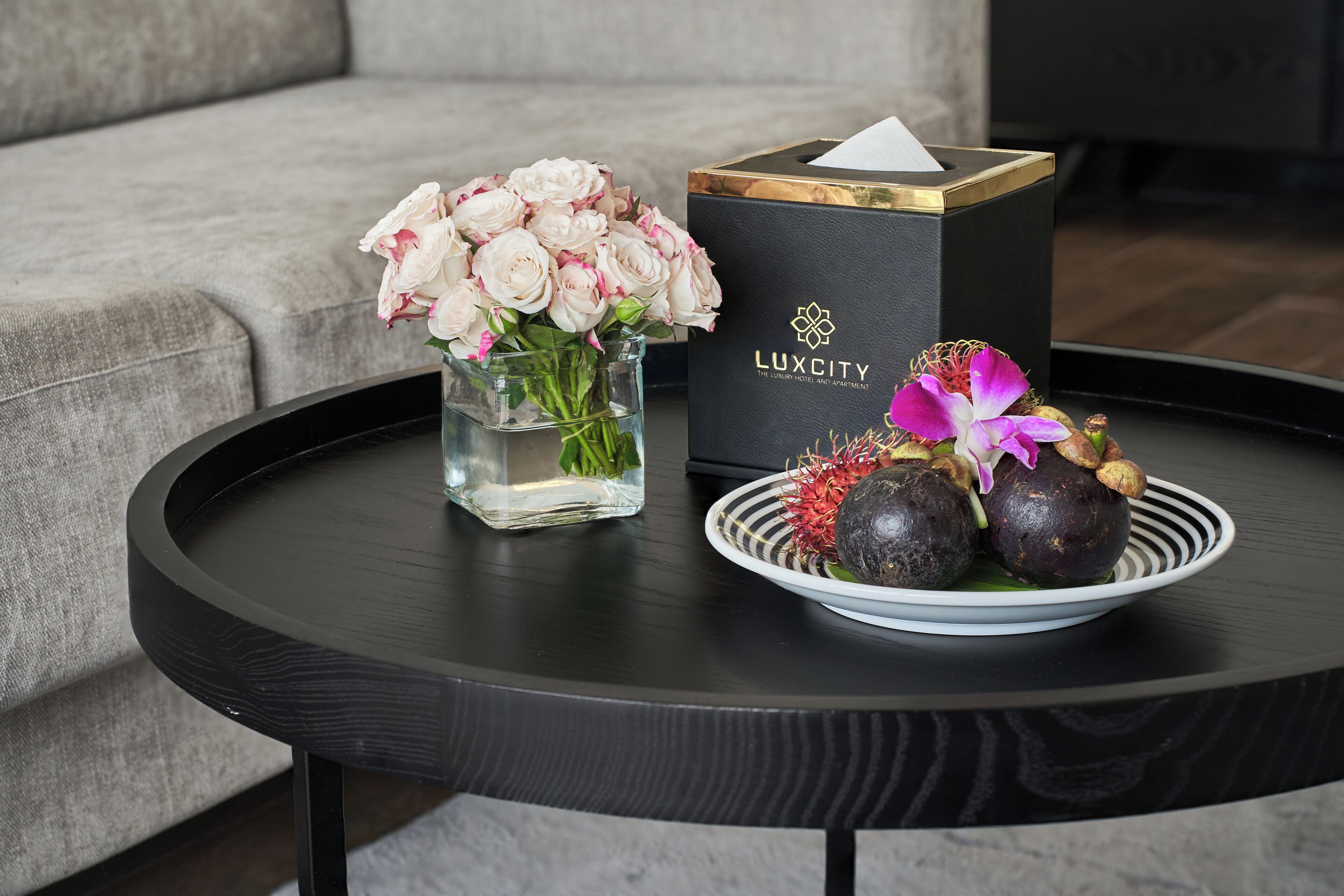 A black table with a vase of white flowers, a black box labeled "LUXCITY," and a plate with decorative items.