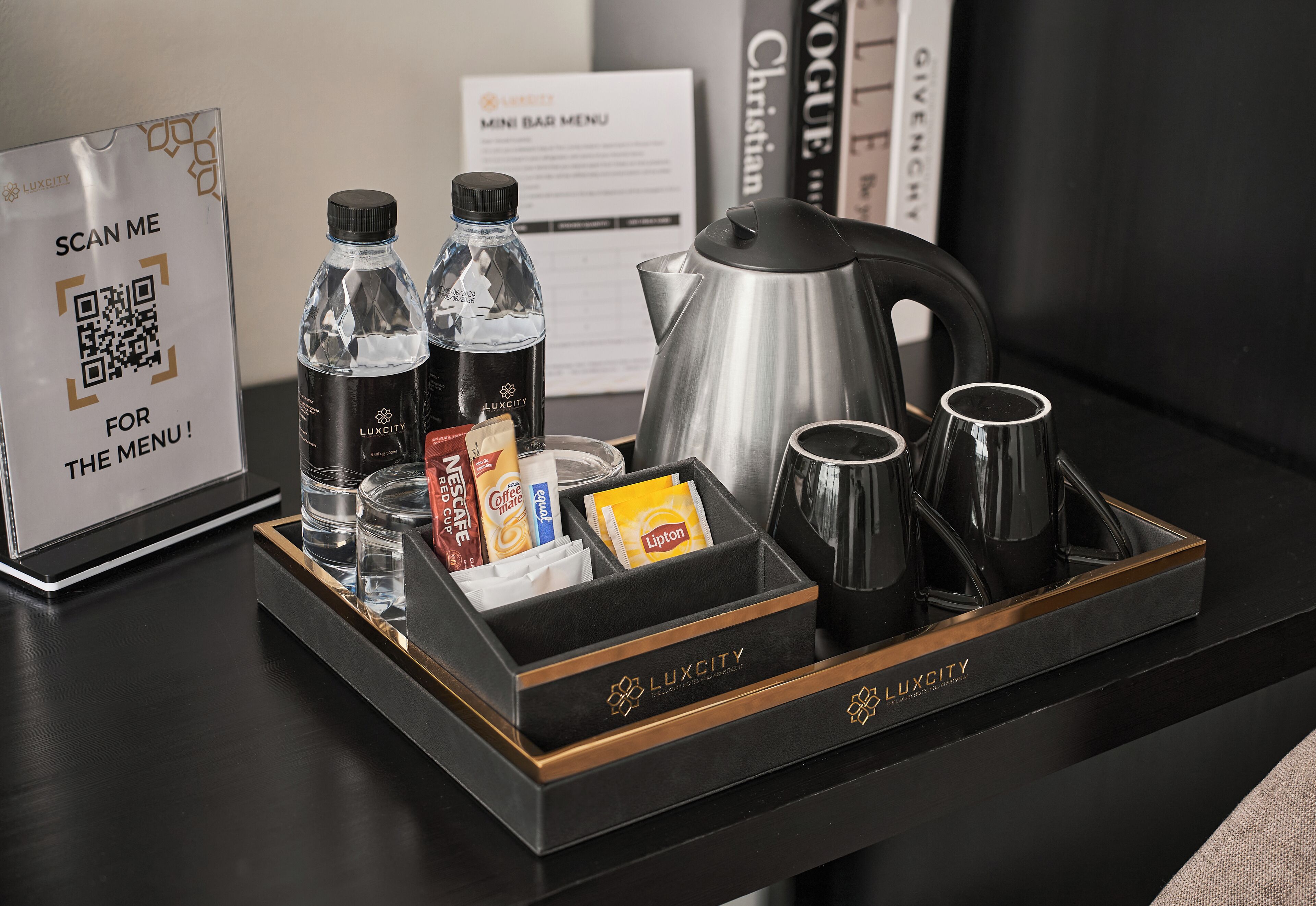 A hotel minibar with a QR code for the menu, a kettle, coffee cups, and bottled water.