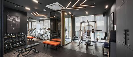 Un gimnasio moderno con equipo de ejercicio, bancos y un estante para pesas instalado en la pared.