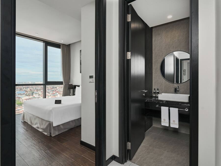 Ein modernes Hotelzimmer mit einem großen Bett, einem Badezimmer mit Waschtisch und Blick auf die Stadt.