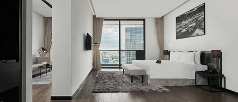 Una habitación de hotel moderna con un amplio ventanal que ofrece vistas a la ciudad, una cama con mesita de noche y un televisor de pantalla plana montado en la pared.