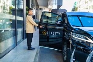 Um veículo de luxo preto com a marca 'LUXCITY' estacionado em frente a um edifício com portas de vidro.