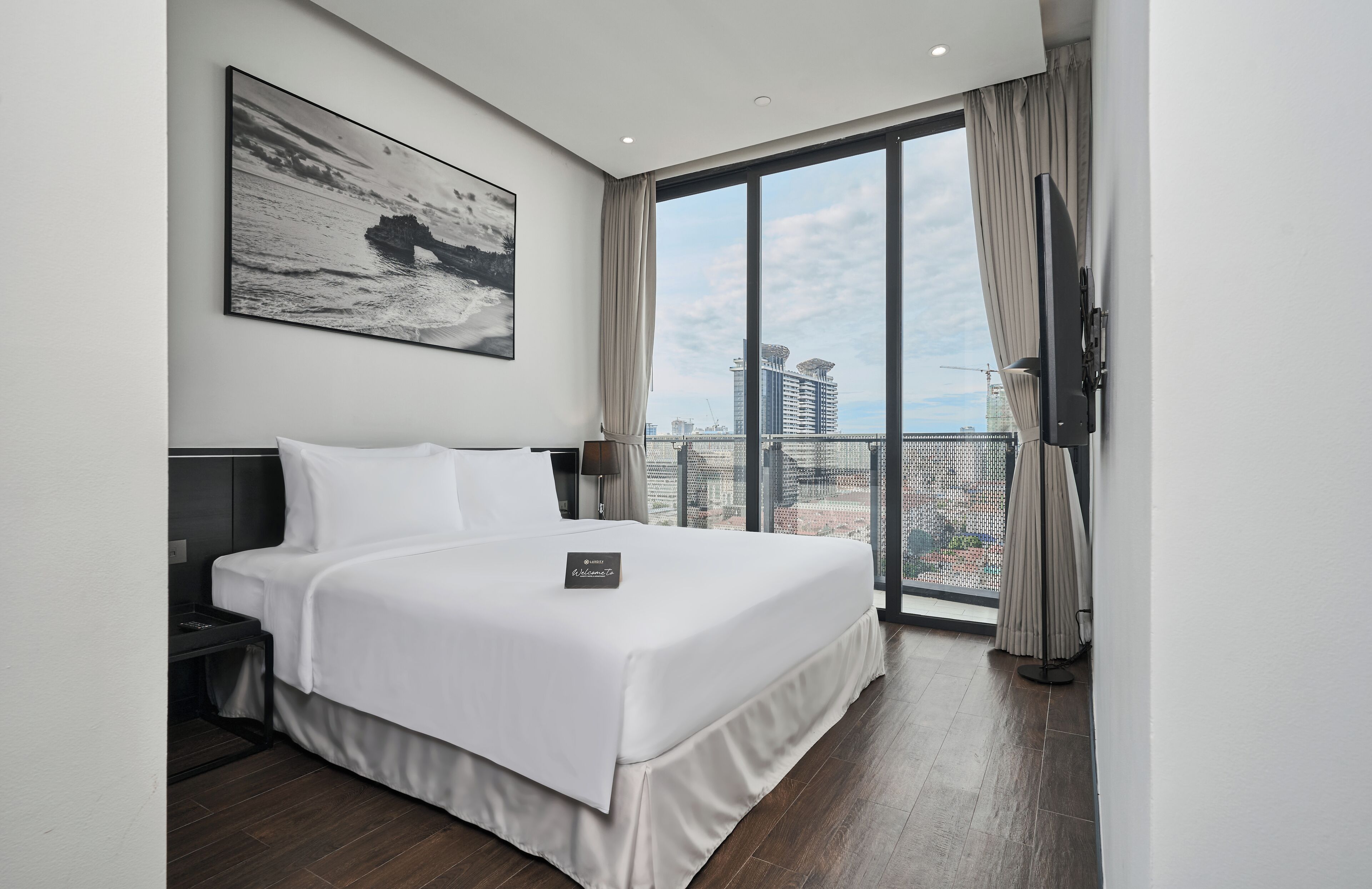 Habitación de hotel moderna con una cama grande, una mesita de noche, un televisor de pantalla plana y un balcón con vistas a la ciudad.