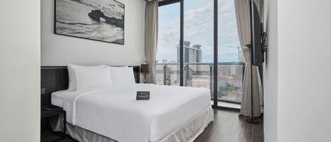 Habitación de hotel moderna con una cama grande, una mesita de noche, un televisor de pantalla plana y un balcón con vistas a la ciudad.