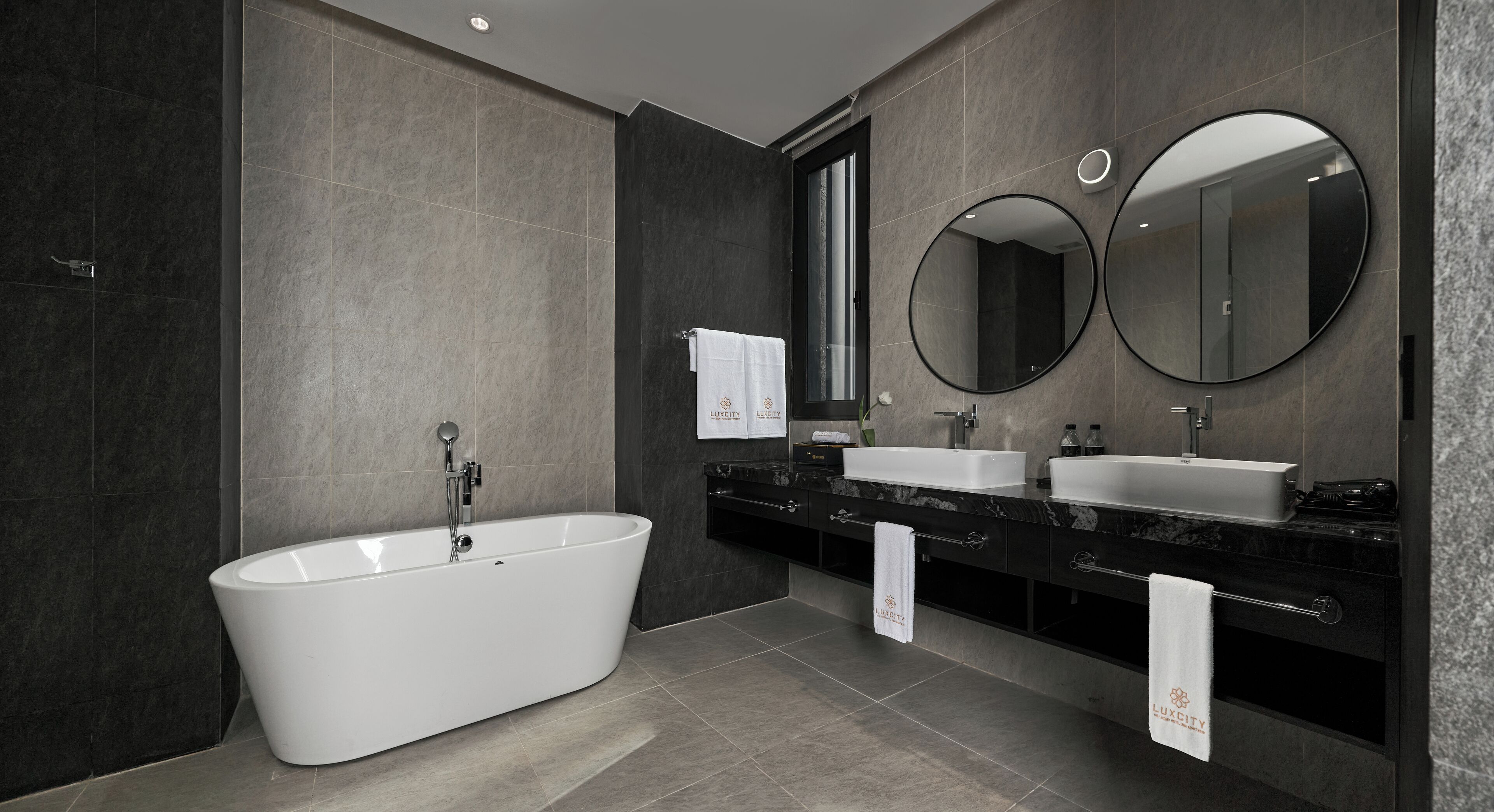 A modern bathroom with a freestanding bathtub, two sinks, and two wall-mounted mirrors.