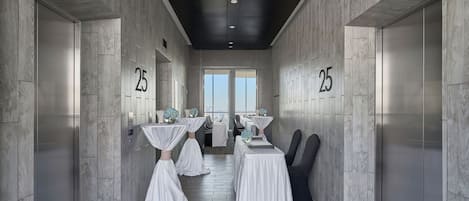 A hallway with numbered doors, tables with white tablecloths, and chairs.