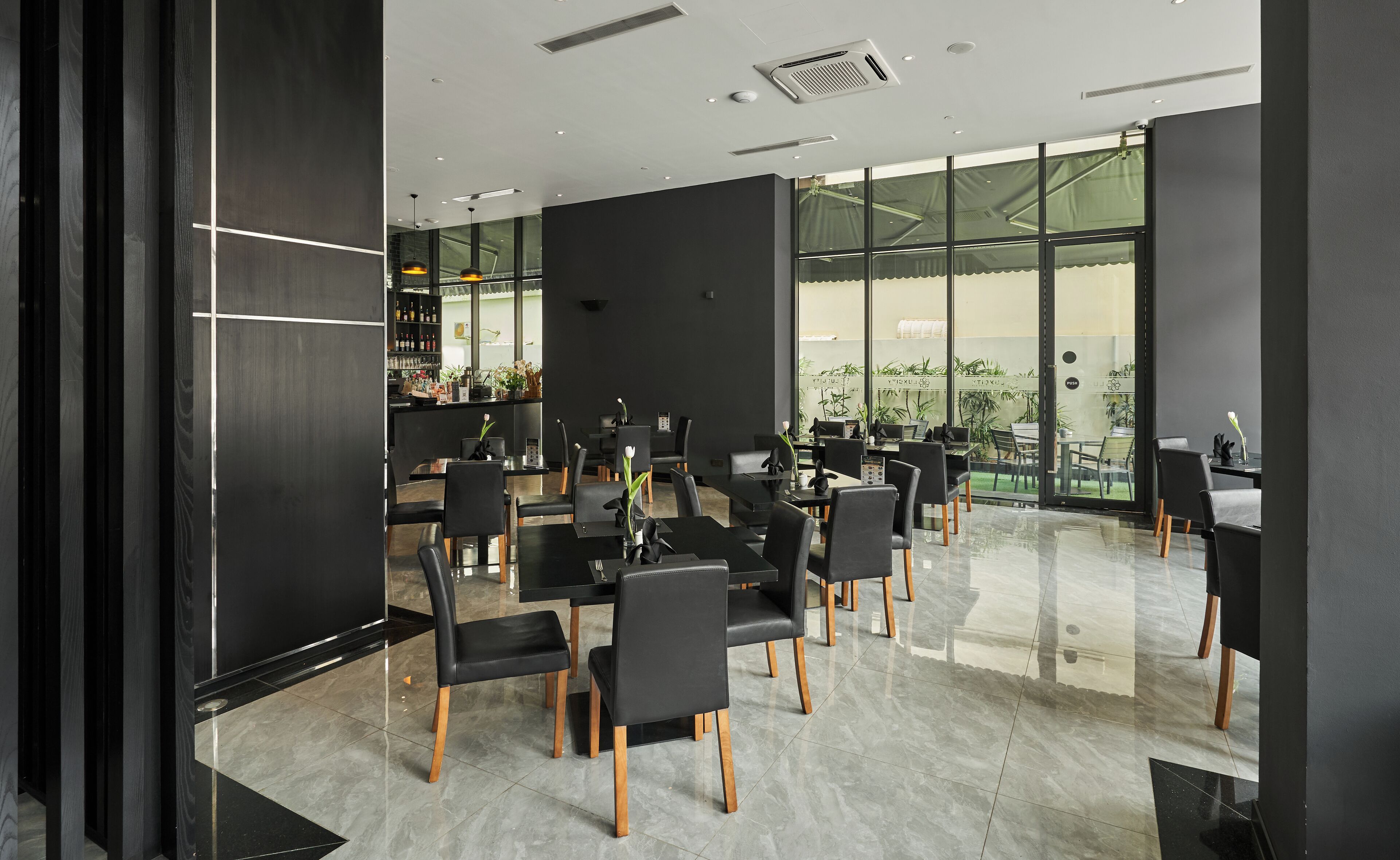 A modern conference room with black chairs and tables, large windows, and a bar area with bottles and glasses.