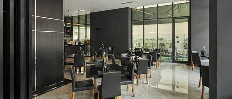 A modern conference room with black chairs and tables, large windows, and a bar area with bottles and glasses.