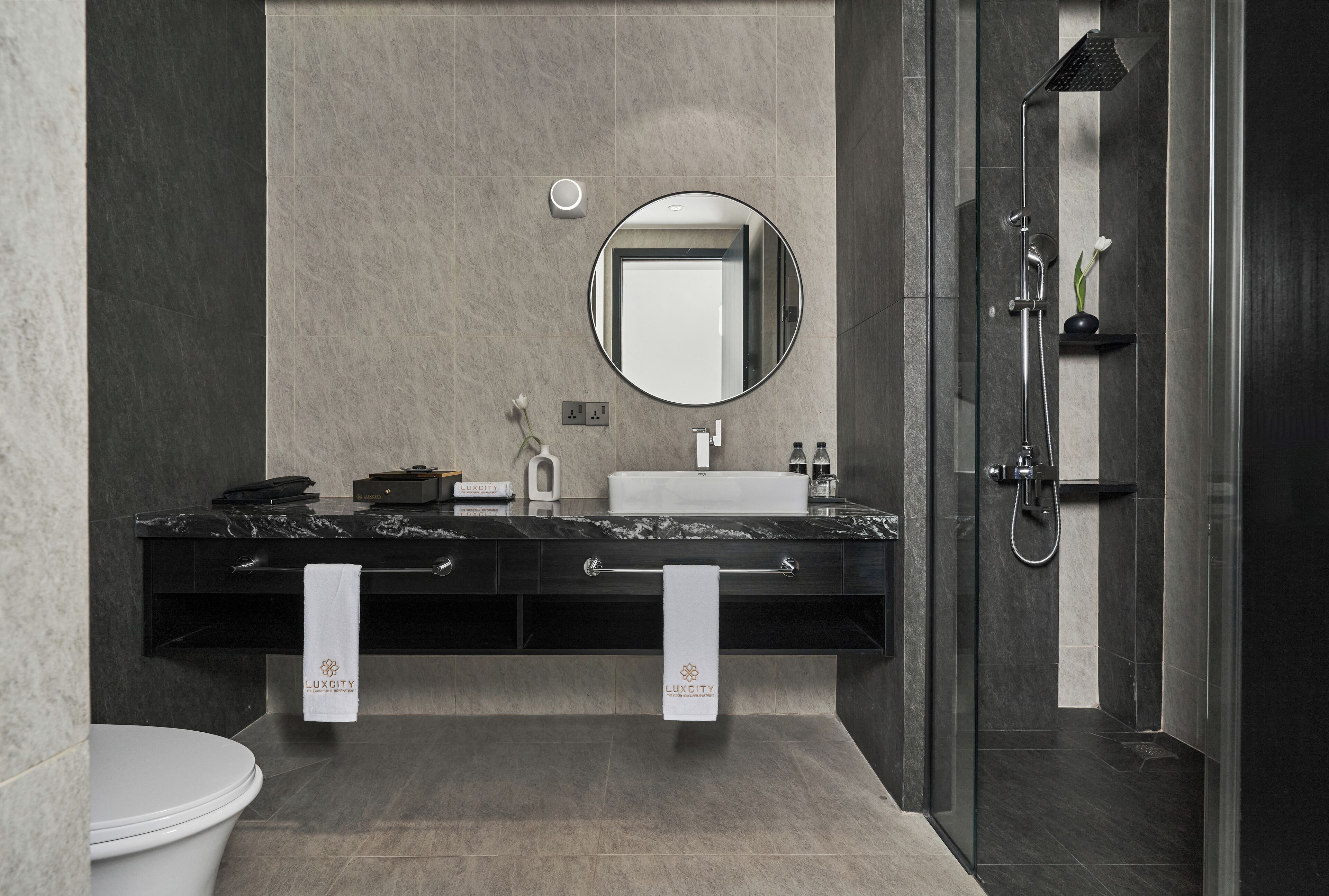 A modern bathroom with a marble countertop, a round mirror, and a glass-enclosed shower.