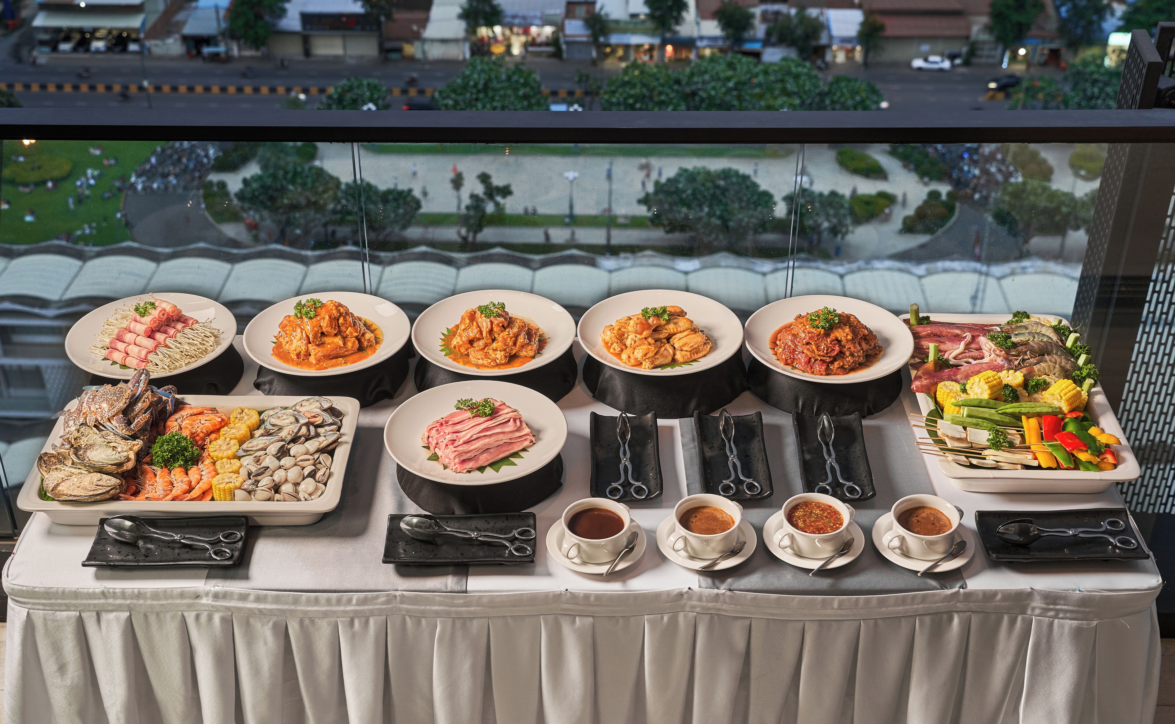 A table with various dishes and drinks, viewed from a window overlooking a cityscape.