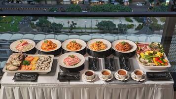 A table with various dishes and drinks, viewed from a window overlooking a cityscape.