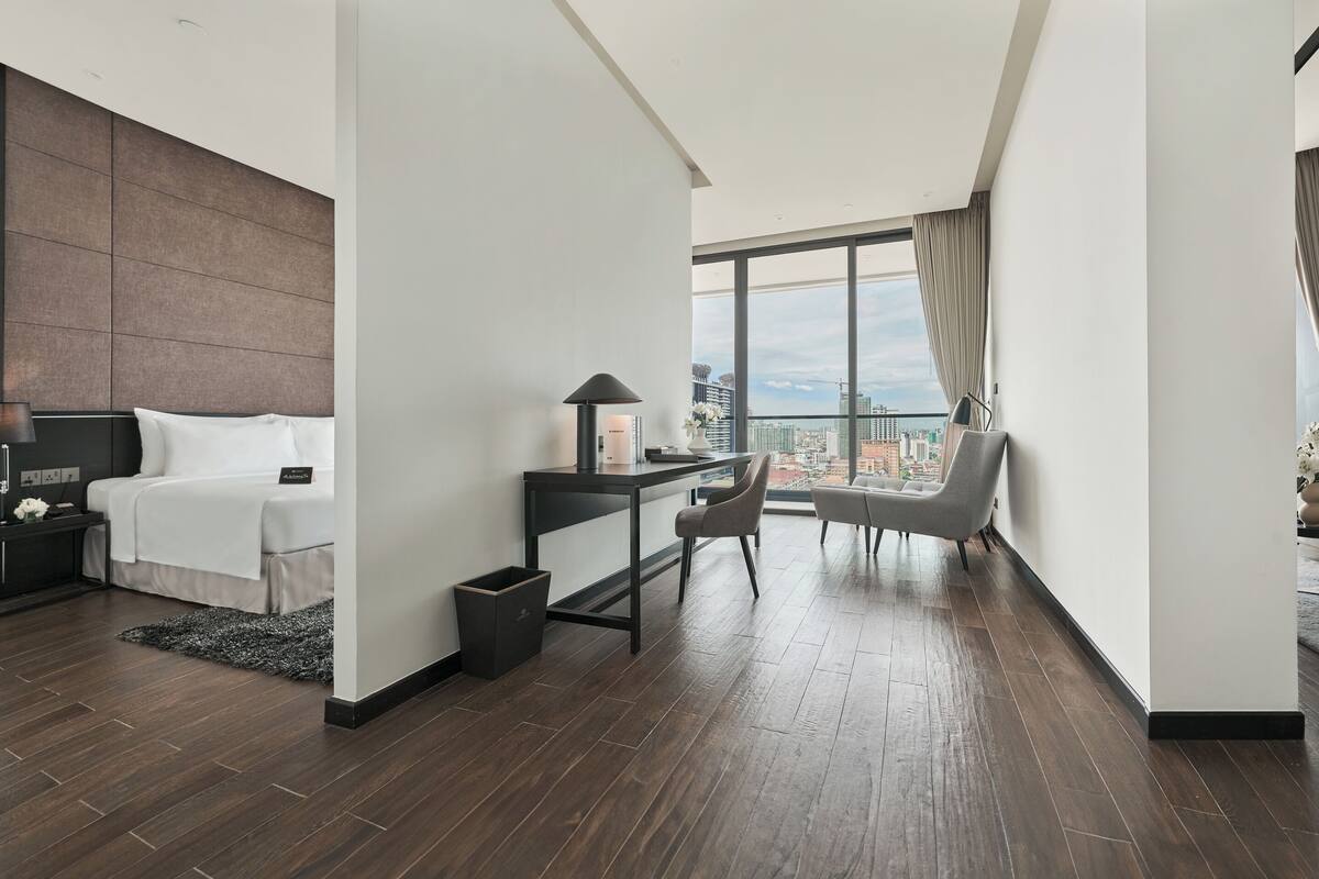 A modern hotel room with a large bed, a desk, a chair, and a view of the city.