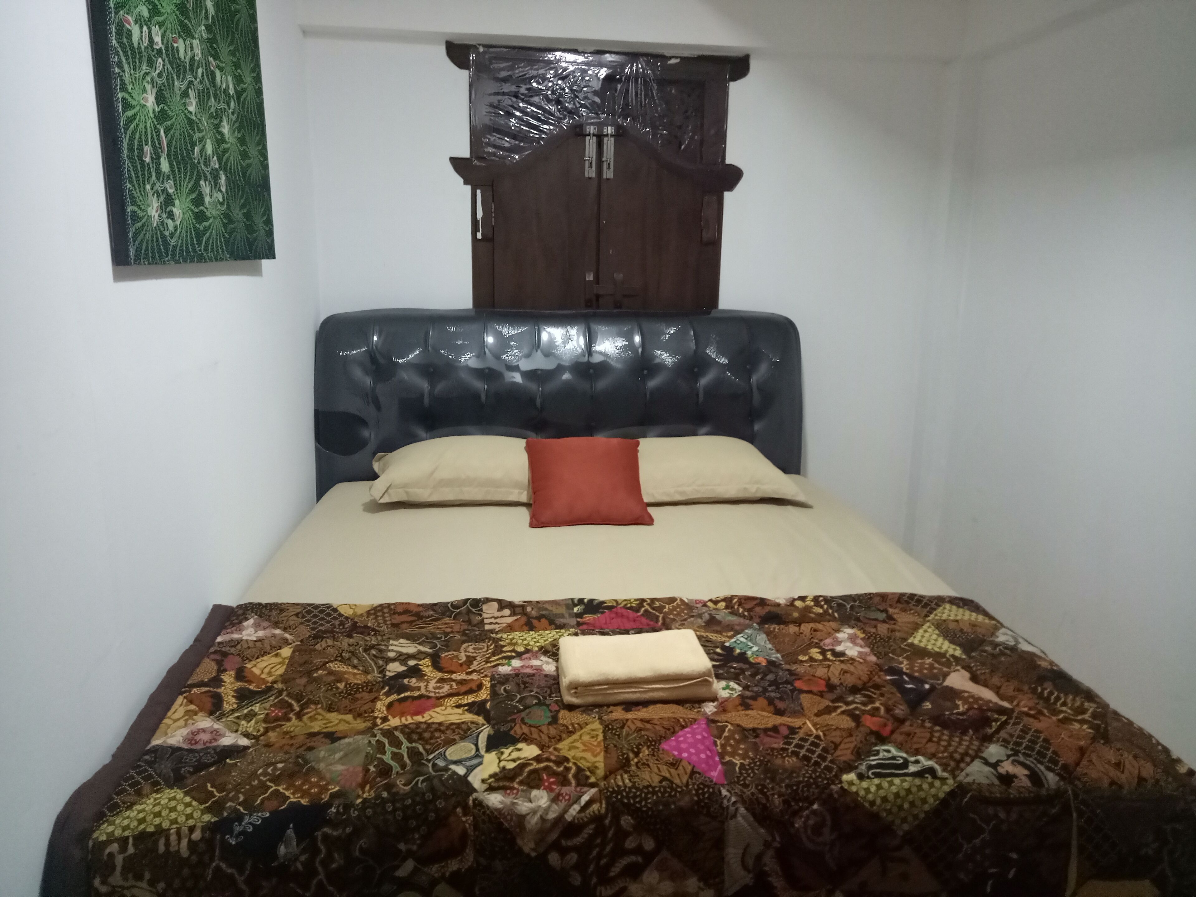 A bedroom with a bed, a wooden wardrobe, and a wall-mounted artwork.