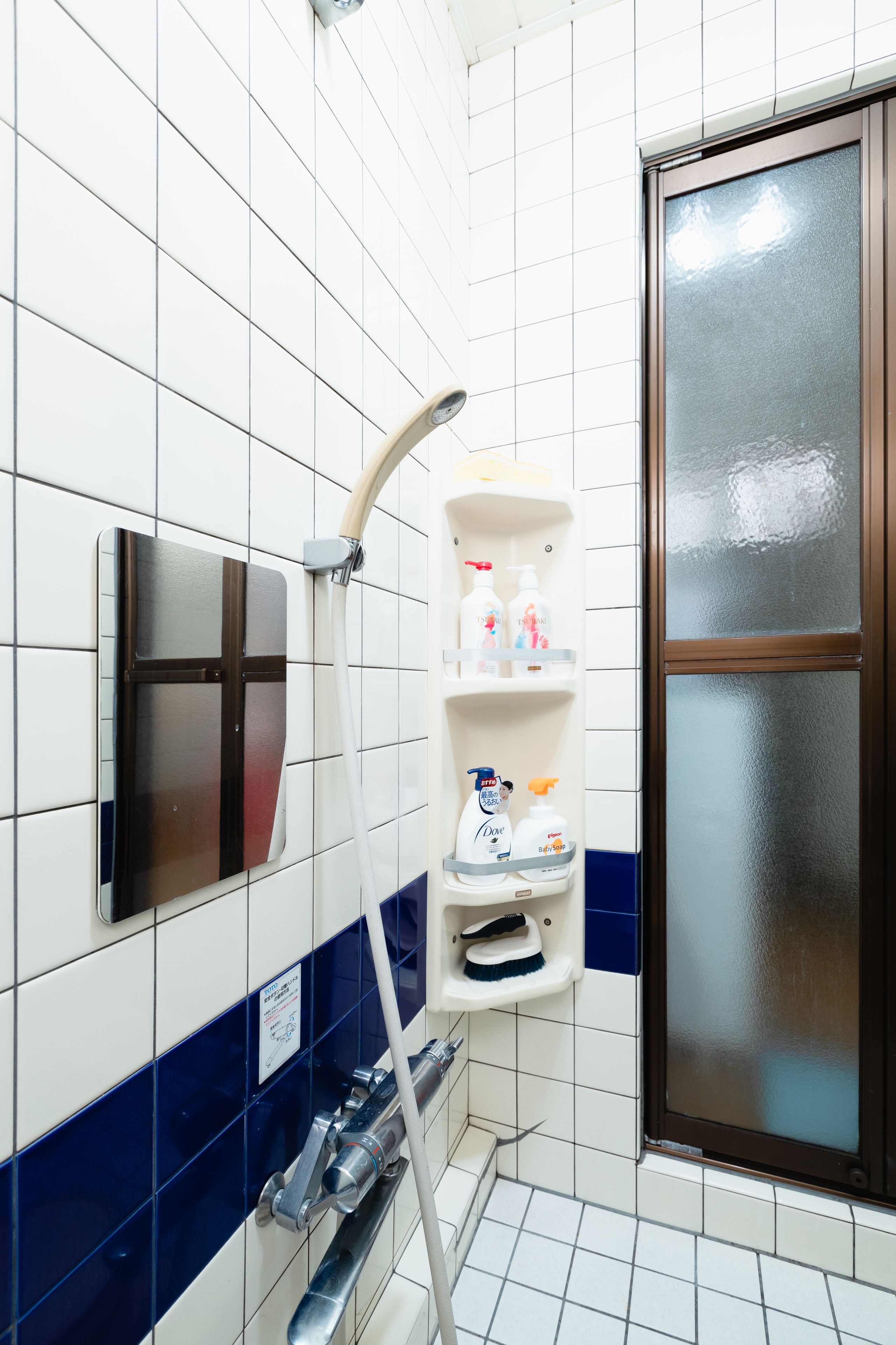 Une salle de bain avec des murs recouverts de carreaux blancs, un mur d’accent bleu, une douche en verre et une étagère contenant des articles de toilette.