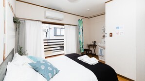 Habitación de hotel con cama, escritorio, silla, lavamanos y ventana con cortinas.