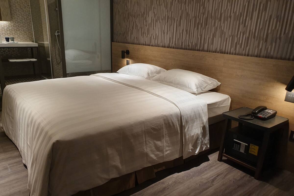 Une chambre d’hôtel avec un grand lit, une table de chevet avec un téléphone et une tête de lit en bois.