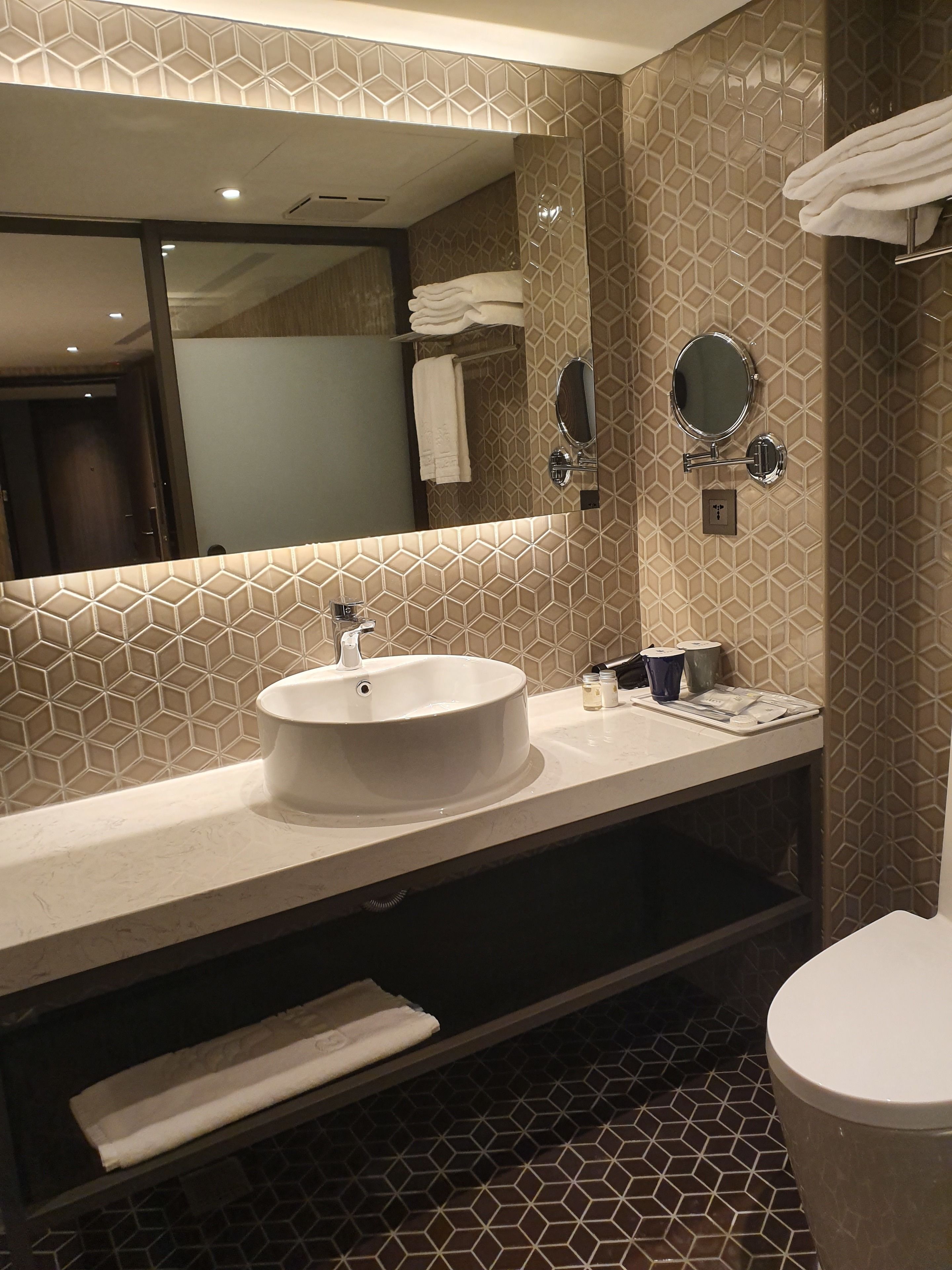 A modern bathroom with a large mirror, a round sink, and a toilet.