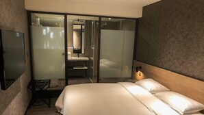 A modern hotel room with a large bed, a desk, and a shower area.