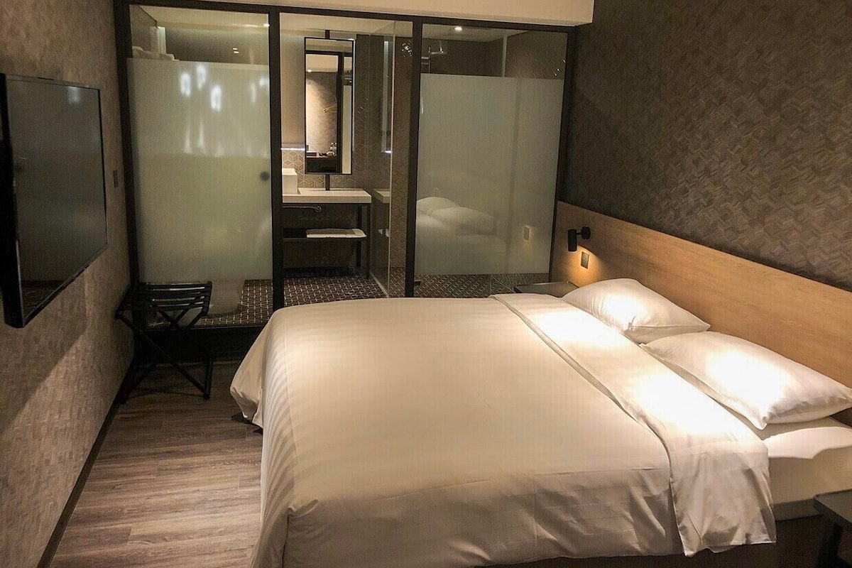 Une chambre d’hôtel moderne dotée d’un grand lit, d’un bureau et d’un espace douche.