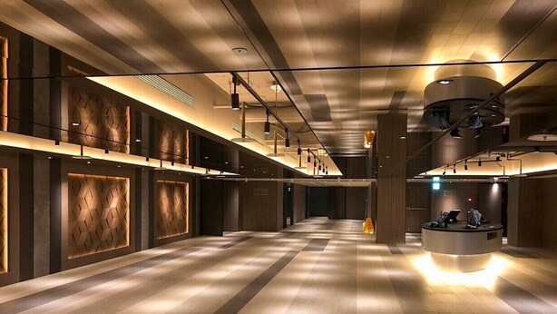 A spacious hotel lobby with a long corridor, a reception desk, and modern lighting fixtures.