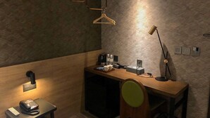 A modern hotel room with a wooden desk, a chair, a desk lamp, a telephone, and a small table with a tray of items.