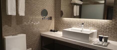 A modern bathroom with a white toilet, a sink with a mirror above it, and a towel rack with folded towels.