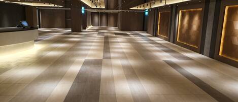 A spacious hotel lobby with a check-in counter, a long reception desk, and a modern ceiling design with recessed lighting.