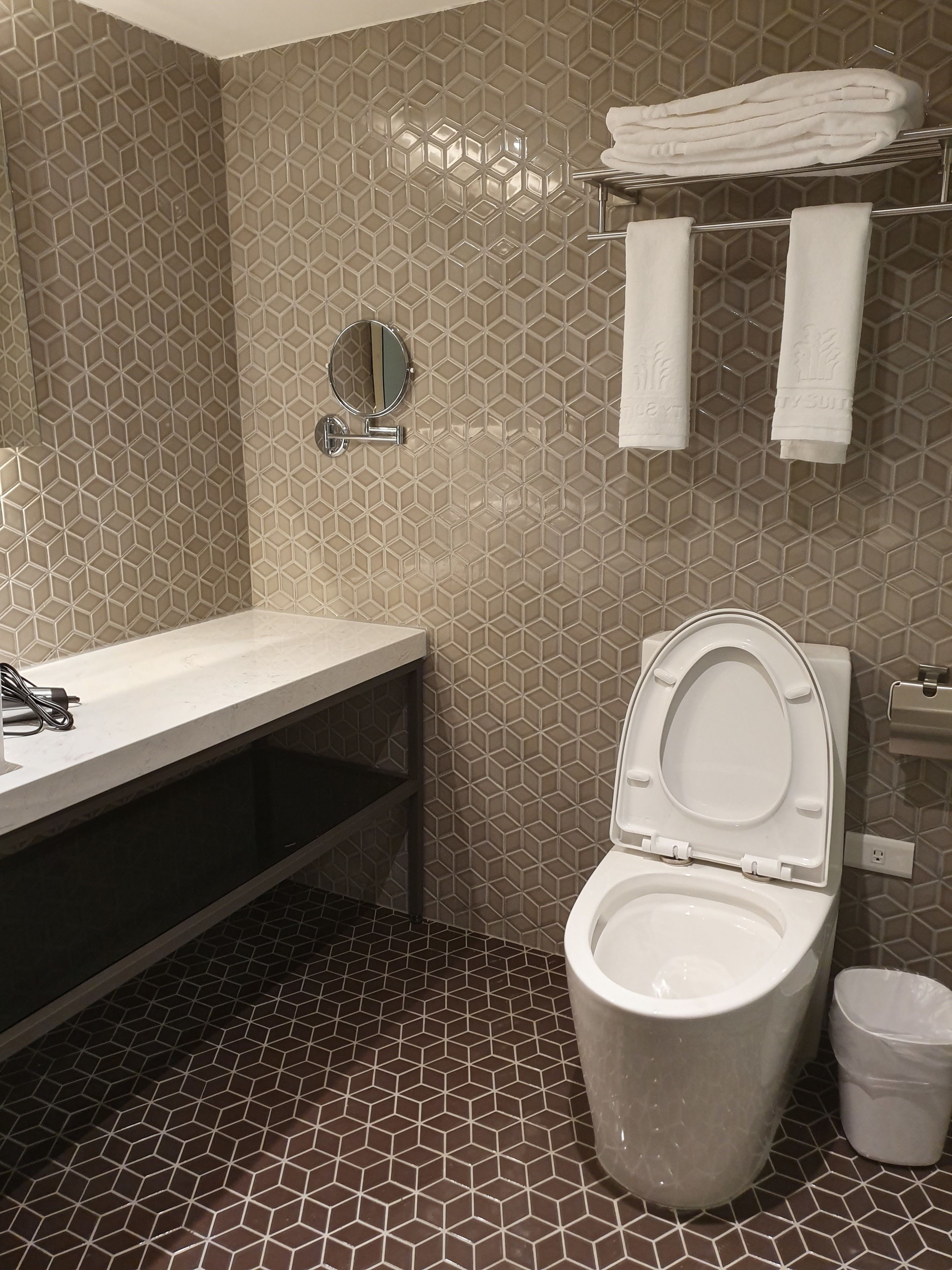 A bathroom with a hexagonal tile pattern, a white sink, a toilet, and a towel rack with folded towels.