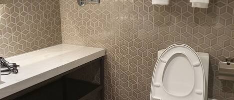 Un baño con un diseño de baldosas hexagonales, un lavamanos blanco, un inodoro y un perchero con toallas dobladas.