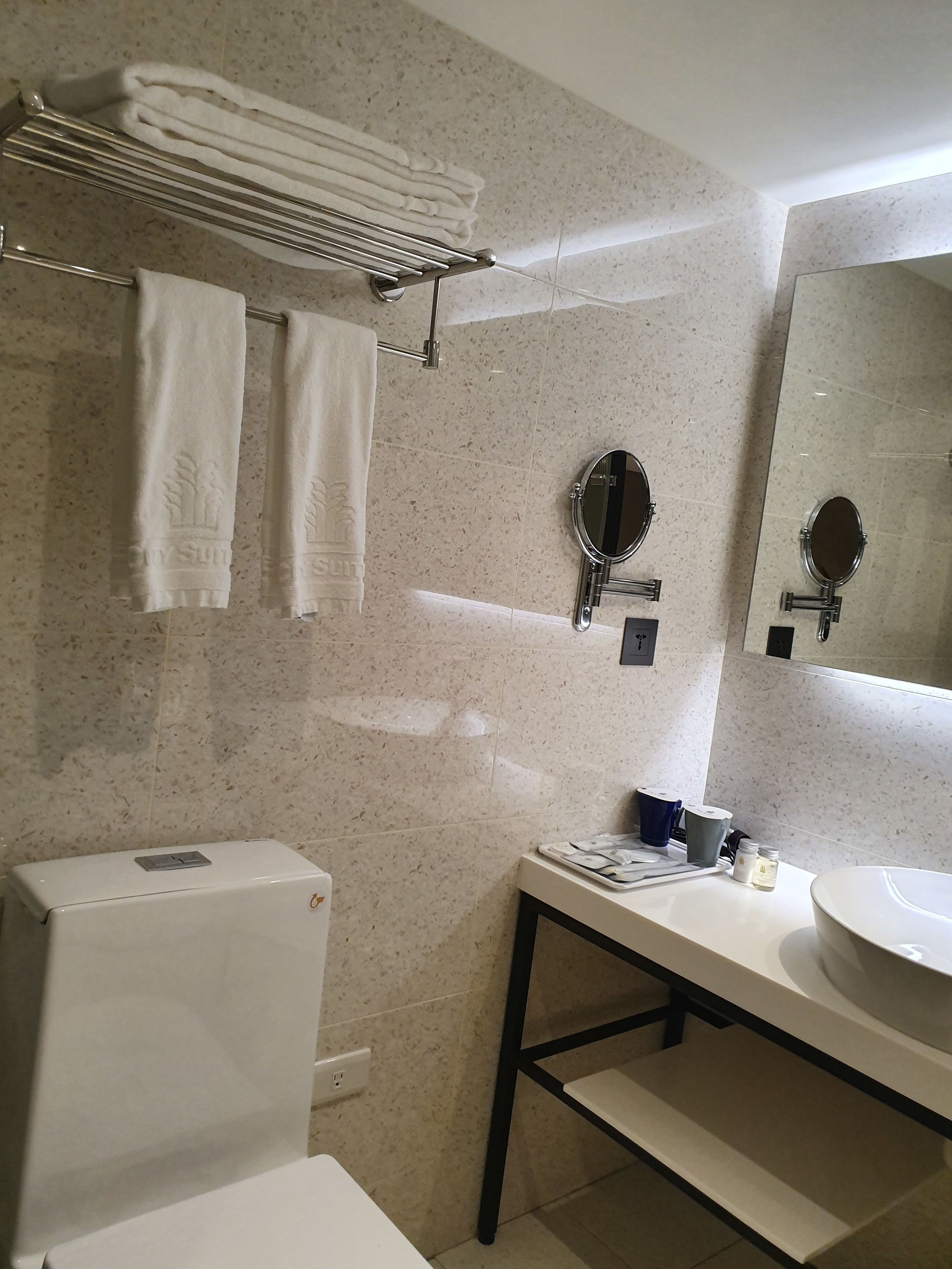 A bathroom with a toilet, sink, and two mirrors. There are towels hanging on a rack and a towel rack above the sink.