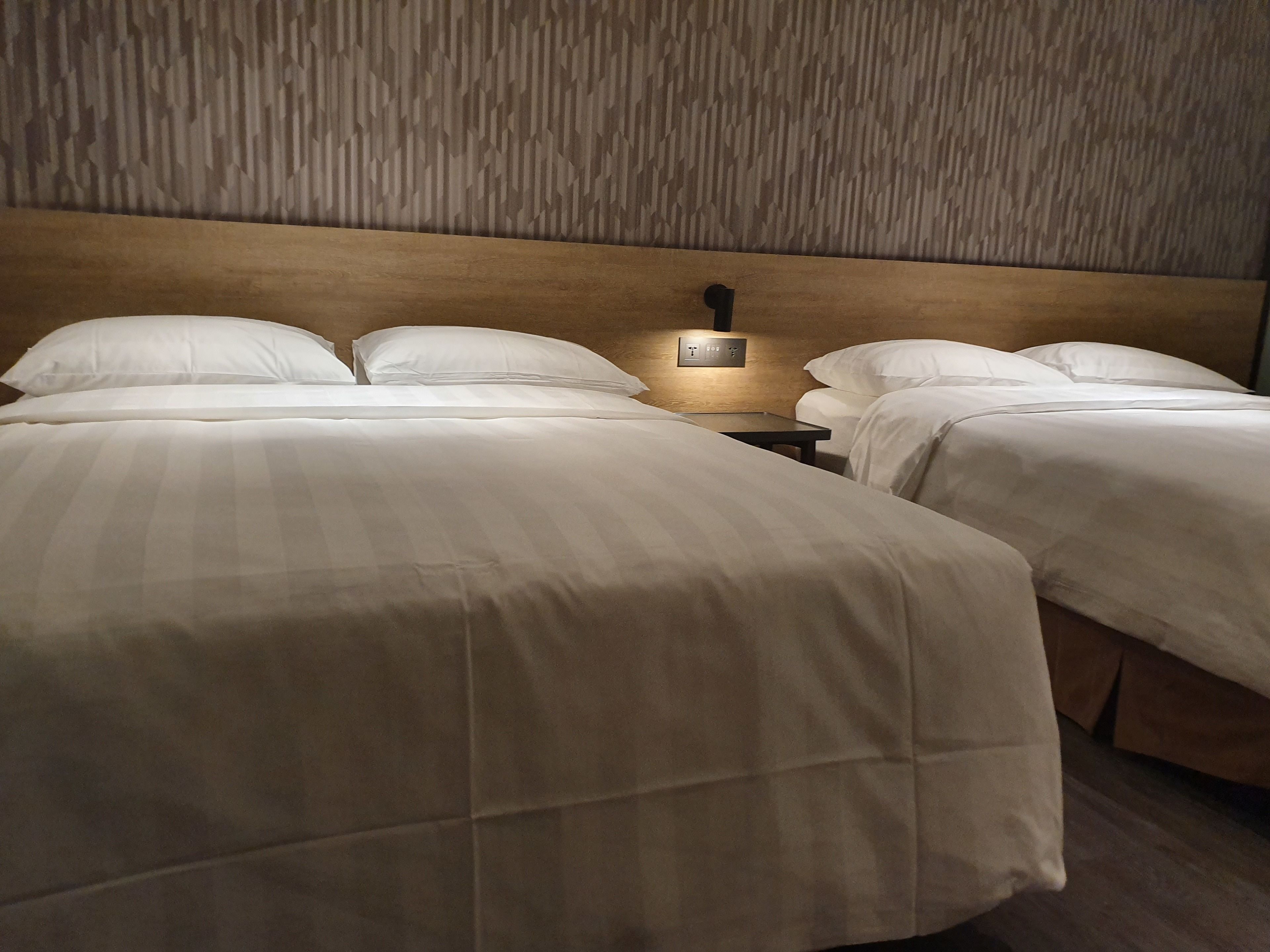 Une chambre d’hôtel avec deux lits, une tête de lit en bois et une table de chevet avec une lampe.