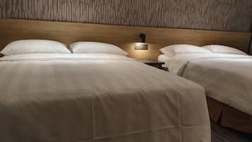 Una habitación de hotel con dos camas, cabecero de madera y una mesita de noche con lámpara.