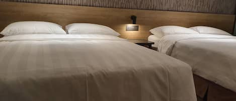 Une chambre d’hôtel avec deux lits, une tête de lit en bois et une table de chevet avec une lampe.
