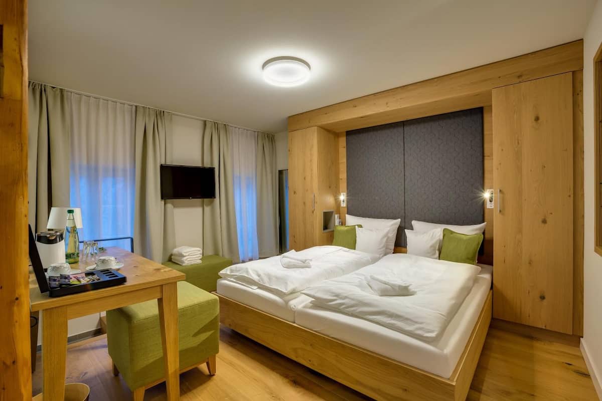 A hotel room with a wooden bed, a desk with a lamp, a television, and a window with curtains.