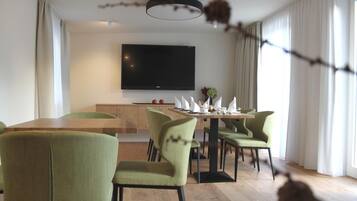 Uma sala de jantar moderna com mesa de madeira e cadeiras estofadas em verde, uma TV de tela plana na parede e uma janela com cortinas.