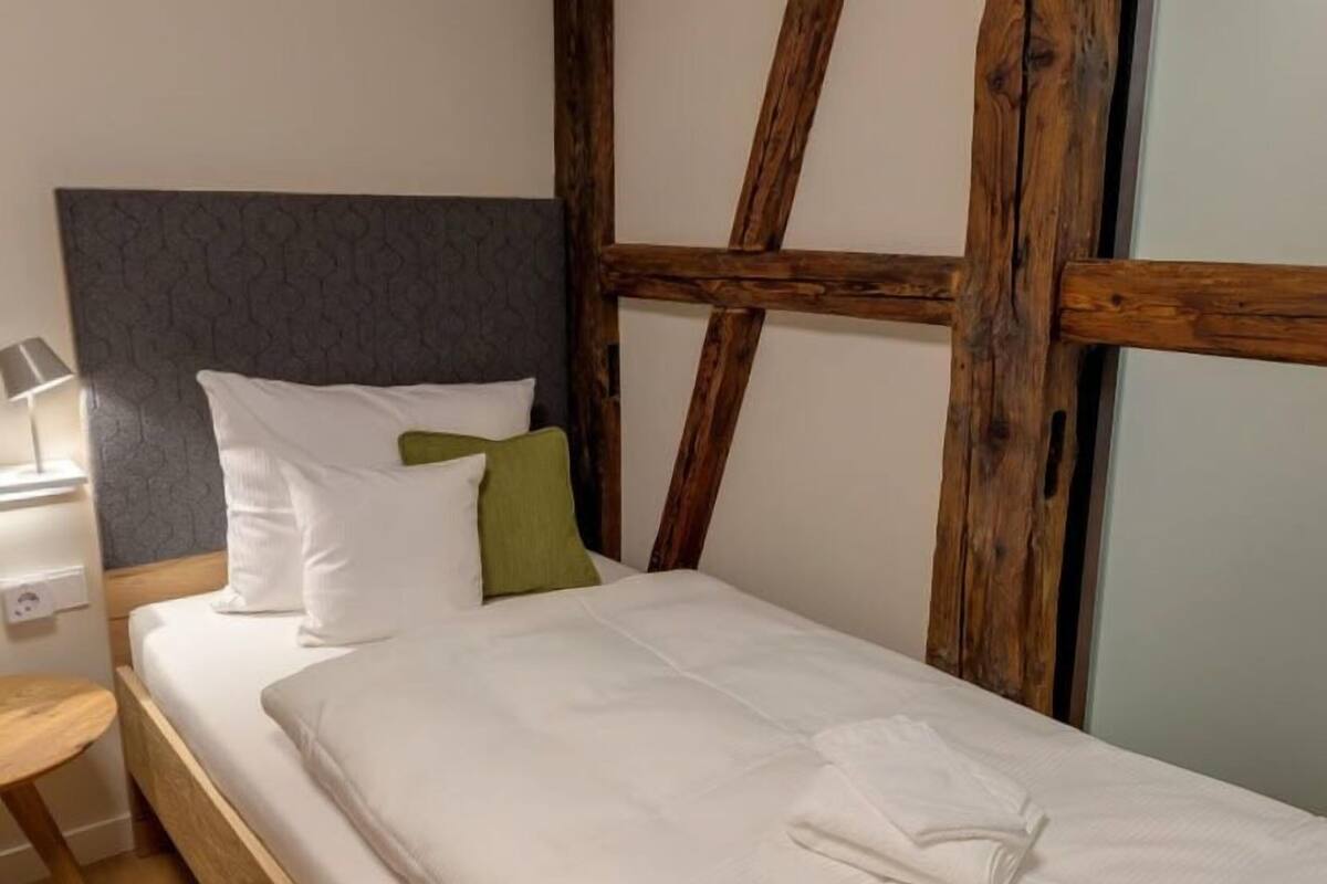 A bed with white bedding, a grey headboard, and wooden beams.
